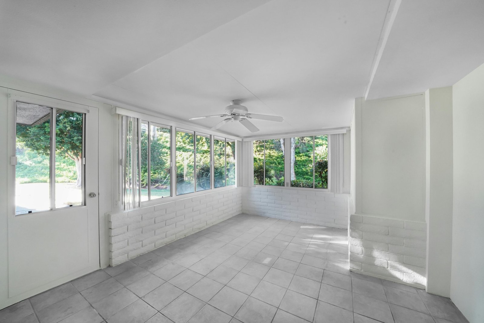 Spacious sunroom with tiled floor, large windows, and ceiling fan, offering outdoor view.