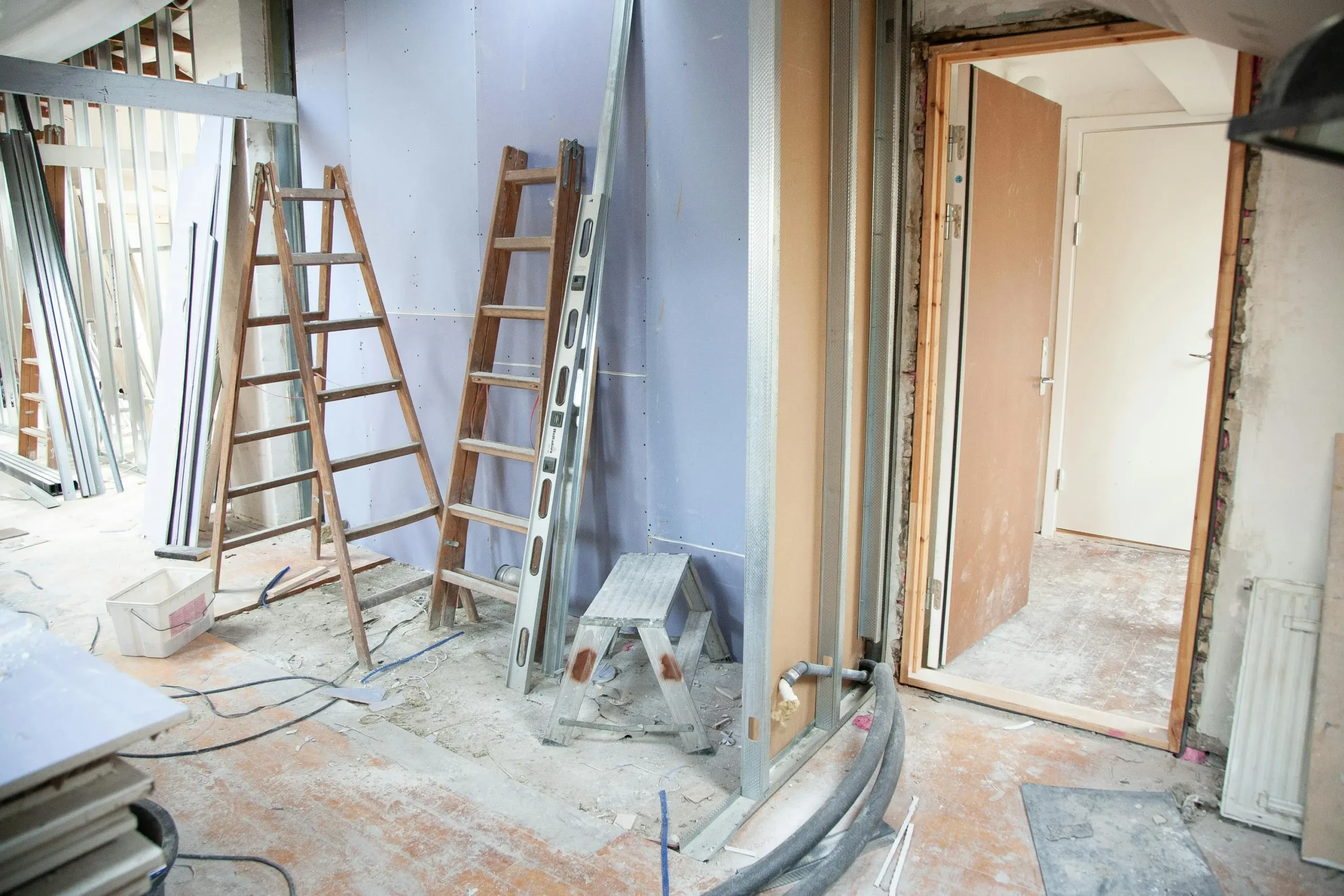 Interior home remodeling in progress with drywall installation, framing, and construction tools.